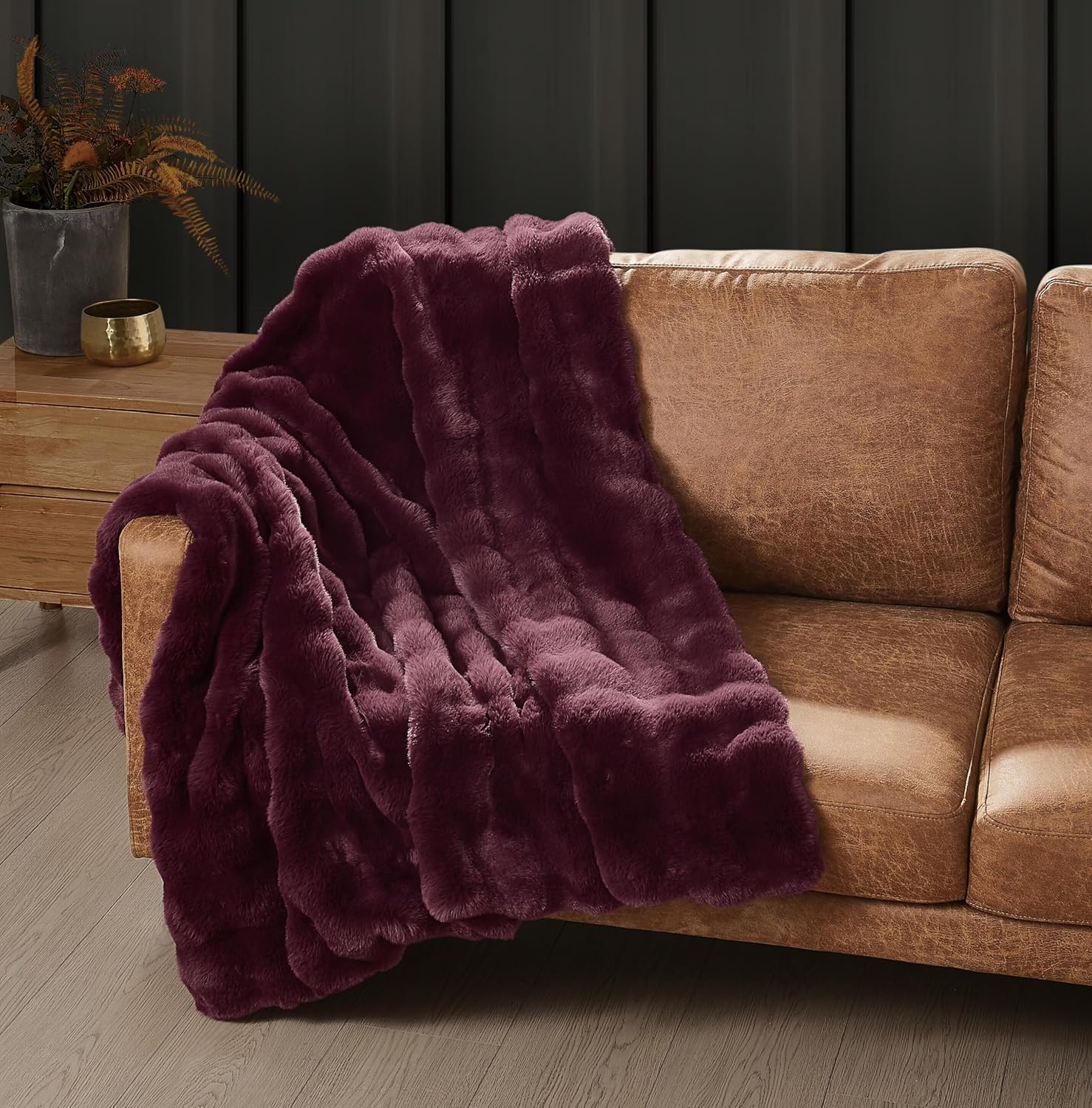 Frye Bubble Rabbit faux fur throw in Fig, a deep wine purple, draped over a cognac leather sofa beside a wooden side table