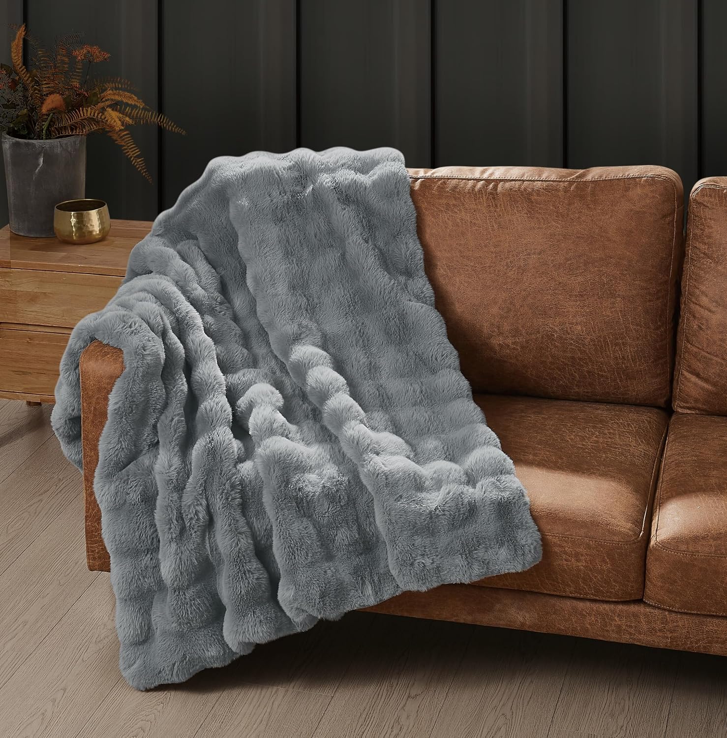 Frye Bubble Rabbit faux fur throw in Grey spread across a cognac leather sofa, the raised bubble texture catching light along the folds