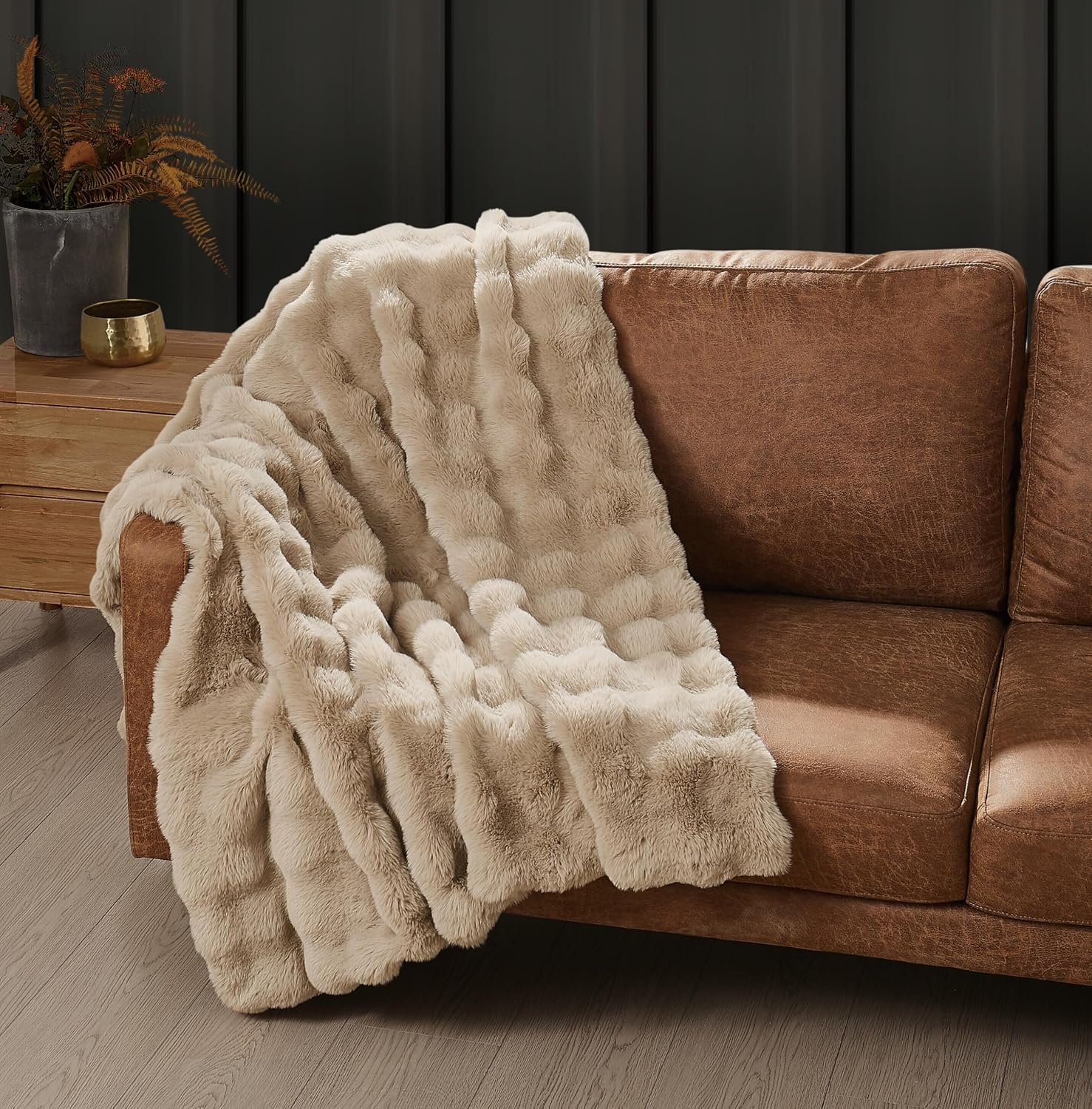 Frye Bubble Rabbit faux fur throw in Tan draped over the arm of a cognac leather sofa, raised bubble pattern visible across the pile